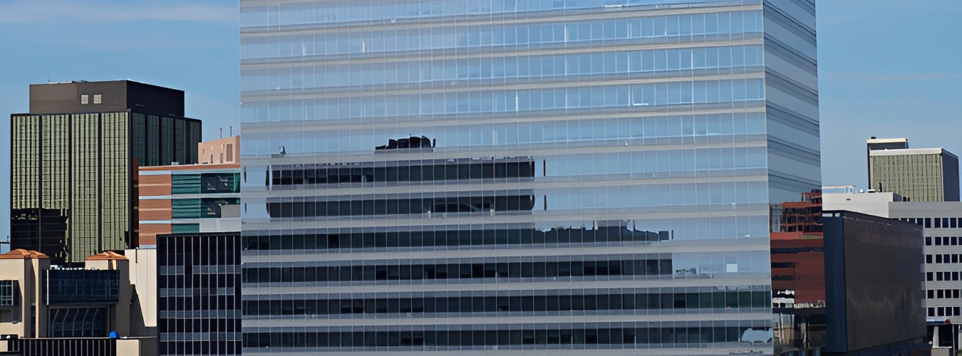 Tall skyscraper with many windows in the middle of a city, surrounded by other buildings with windows, a fence