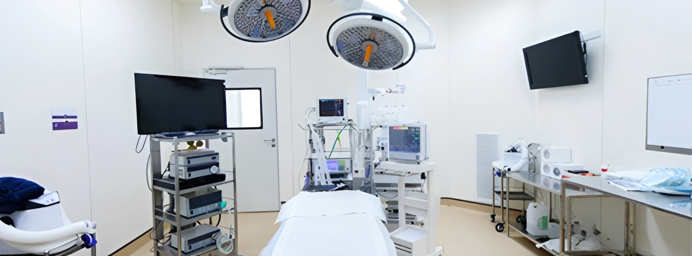 Hospital room with a bed, chairs, monitors, electronic devices, a whiteboard, a television, a door, and various other objects
