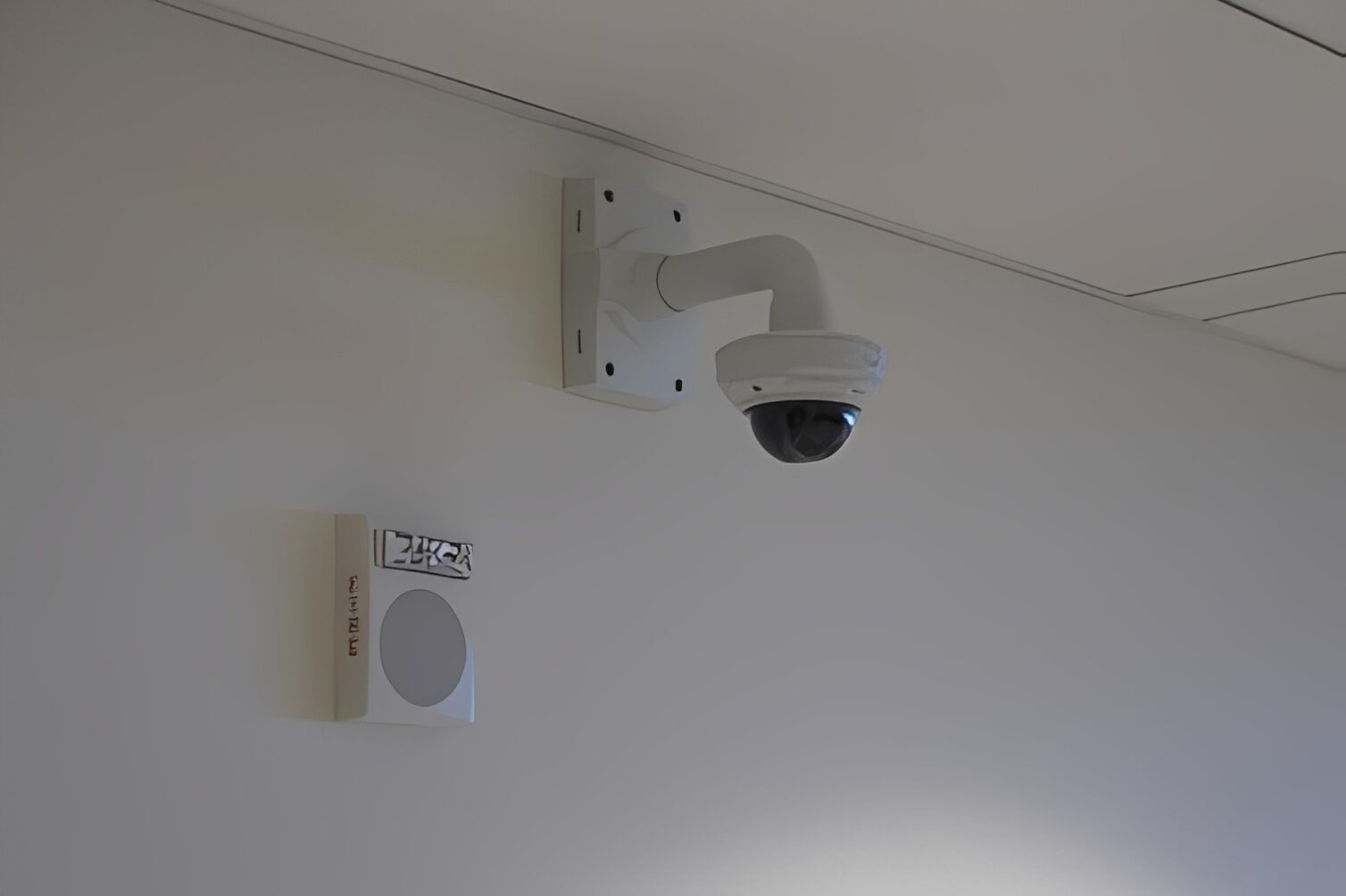 Security camera mounted on the wall of a room, with a white object attached to it